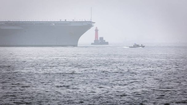 Egy amerikai haditengerészeti repülőgép-anyahajót kísérnek ki Yokosuka kikötőjéből a japán Tokió-öböl ködébe.. - Fotó, kép