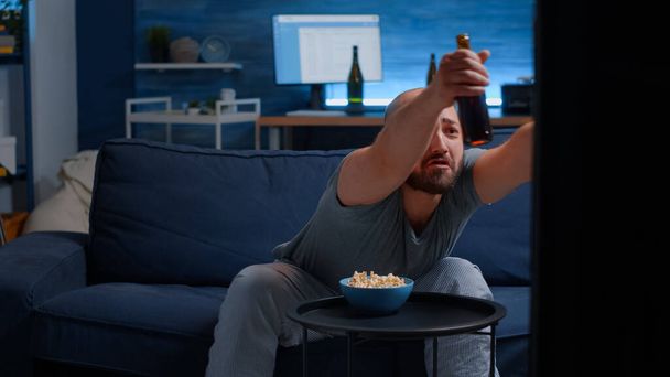 男を保持リモートコントローラー食べるポップコーン見スポーツ上のテレビ - 写真・画像