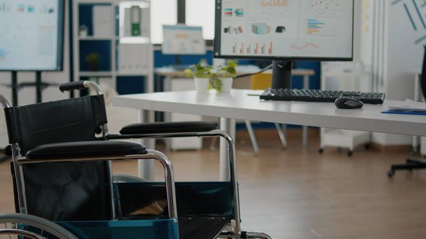 Wózek inwalidzki zaparkowany w pustym pomieszczeniu biurowym przy biurku w firmie start-up - Zdjęcie, obraz