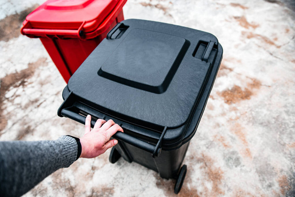 Hand holding black waste container. - 写真・画像