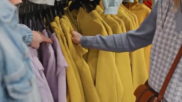 右のサイズを探している衣料品店でレールにかかって鮮やかな色の並べ替えのパーカーの認識できないカップルのクローズアップ - 映像、動画
