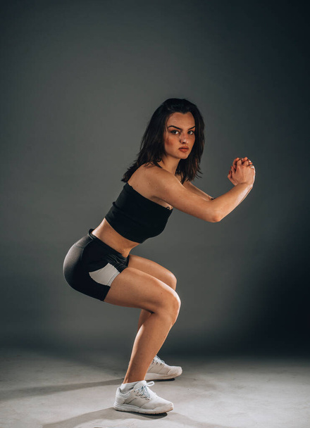 Sportlich schöne Frau streckt die Beine auf der Seite. Ganzkörperporträt isoliert über dunklem Hintergrund. - Foto, Bild