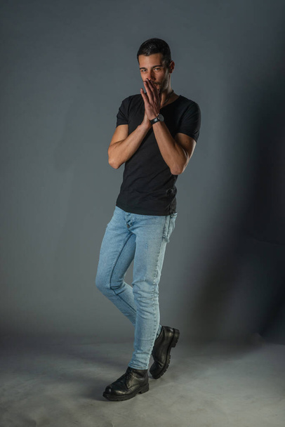 Φωτογράφηση στούντιο ενός όμορφου άνδρα που ποζάρει με τζιν και μαύρο πουκάμισο - Φωτογραφία, εικόνα