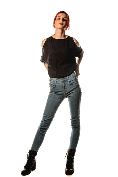 Elegante mujer joven con pantalones de mezclilla azul y camiseta negra contra la pared blanca - Foto, Imagen