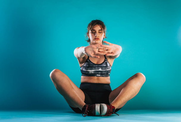 Ritratto di una forte atleta adulta che fa esercizi di stretching isolata su sfondo blu - Foto, immagini