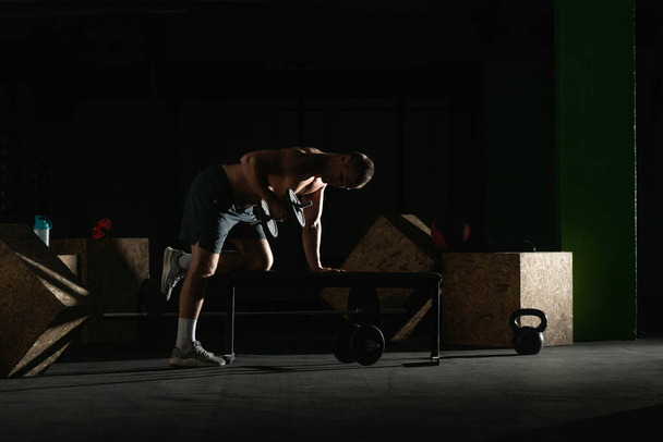 Athletic caucasian man doing a dumbbell triceps kickback with his right arm on a horizontal bench. - Foto, Imagen