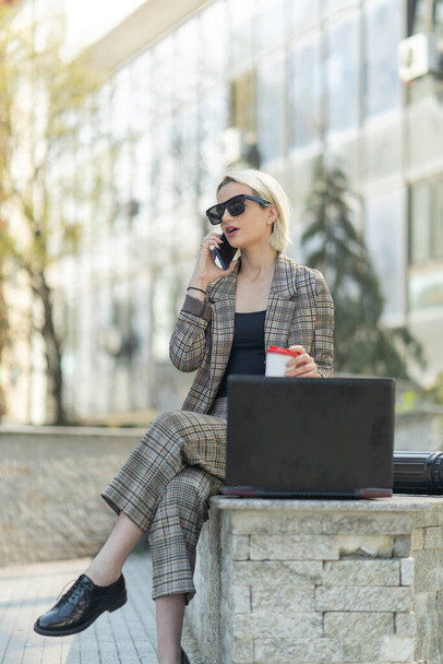 ビジネスマンの女性は晴れた日に彼女のパートナーと彼女の携帯電話で話している間、彼女のラップトップで働いています - 写真・画像