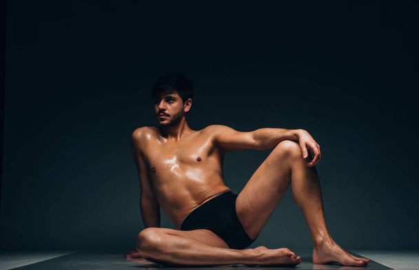 Very sexy young male muscular model in black underwear posing in dark studio - Photo, Image