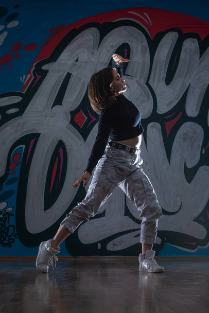 Силуэт молодой женщины-хип-хоп танцовщицы (брейк-дансер), танцующей на фоне студии граффити. Цвета контраста. - Фото, изображение