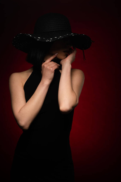 Mysterie meisje is poseren in zwart jurk op rode achtergrond in studio - Foto, afbeelding