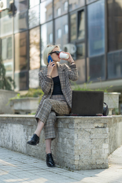 Businesswoman is talking on the phone with her partners while drinkingher coffee on a sunny day - Photo, Image