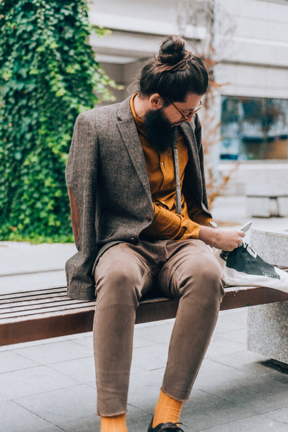 Fashionable male wearing stylish modern clothing holding a phone at the city square - Photo, image