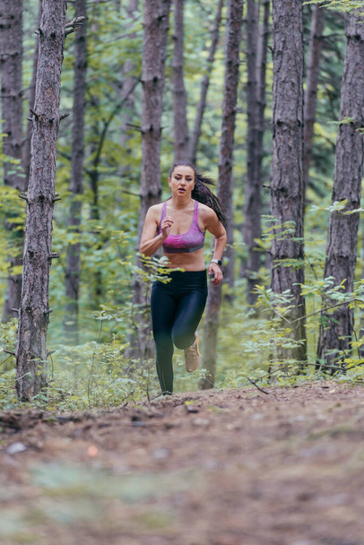 Jeune fille sportive athlétique fait du jogging à l'extérieur sur un sentier forestier - Photo, image