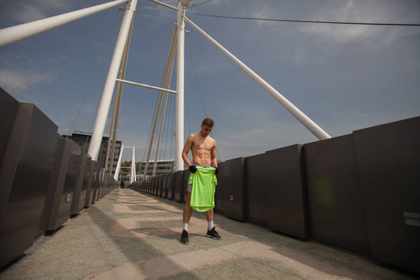 Δυνατός άντρας παίρνει το πουκάμισό του στη μέση της γέφυρας. - Φωτογραφία, εικόνα