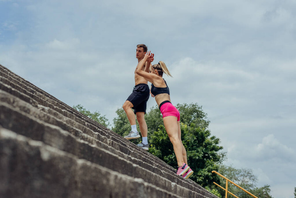 Níže pohled na mladé mužské a ženské sportovce skákání nahoru na venkovní schodiště - Fotografie, Obrázek