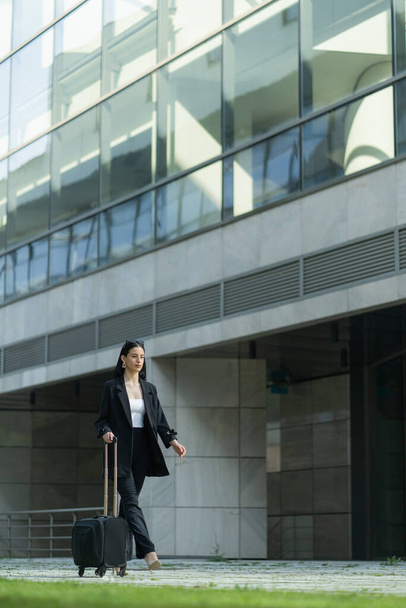 Ελκυστική επιχειρηματίας περπατά με την ταξιδιωτική τσάντα της προς την εταιρεία - Φωτογραφία, εικόνα
