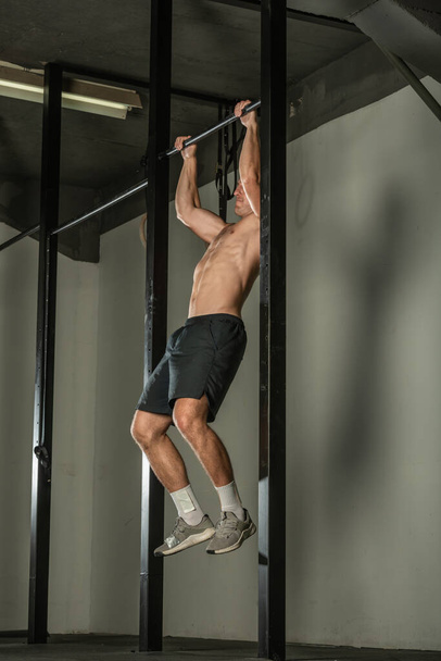 Knappe bodybuilder doet pull-ups op horizontale balk in een moderne fitnessruimte. - Foto, afbeelding