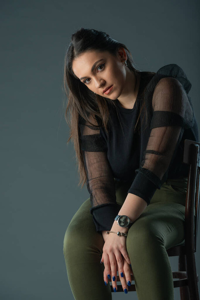 attractive brunette model sitting on a old chair posing and looking at camera on grey background - Zdjęcie, obraz