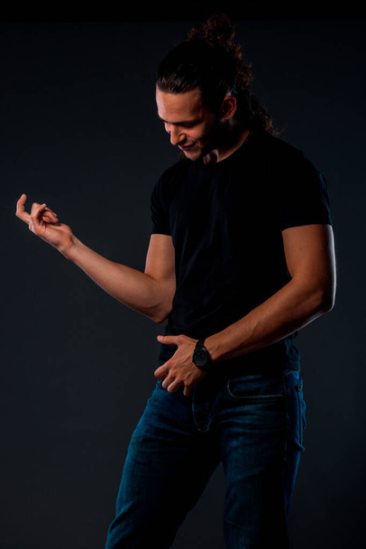 Cool young man dressed in black t-shirt posing in modern studio against black background - Photo, Image