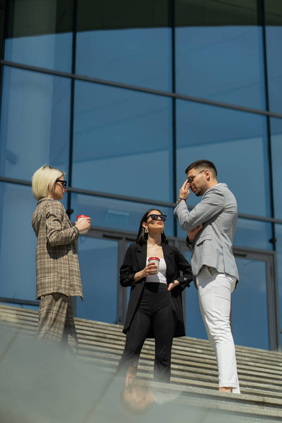 Tre persone di affari urbani stanno parlando in una giornata di sole mentre bevono caffè - Foto, immagini
