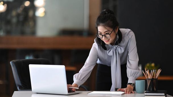 Empresaria en gafas de vista de pie en su espacio de trabajo y trabajando en el ordenador portátil. - Foto, Imagen
