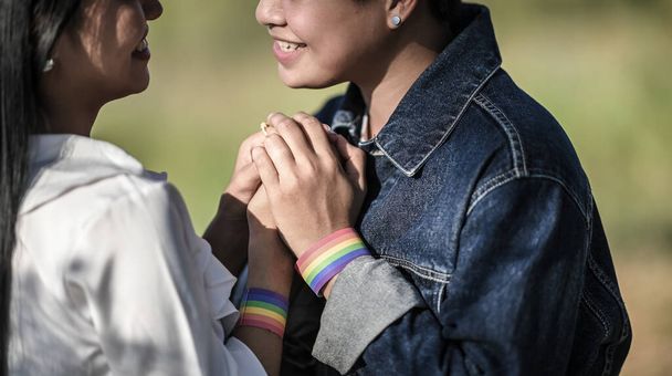 Cropped shot of young LGBT Lesbian holding her lover hand at the beautiful park with the blurred green grass as background. LGBT Happiness couple concept. - Photo, image