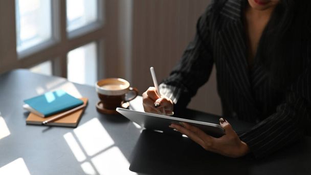 Cropped image of businesswoman holding using computer tablet with stylus pen while sitting at working table. - 写真・画像