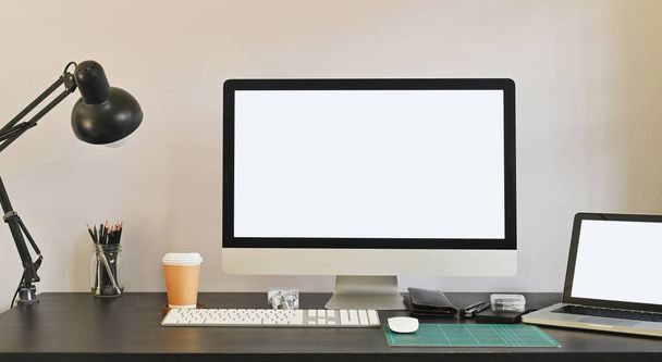 Fotografie bílého prázdného obrazovkového počítače a bílého prázdného obrazovkového notebooku skládajícího se na stůl, včetně lampy, šálku kávy, držáku tužky na myši a osobního vybavení. Moderní koncepce pracovního stolu. - Fotografie, Obrázek