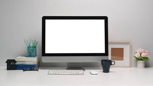 Vista frontal de la computadora moderna con pantalla en blanco y suministros de oficina en escritorio de oficina blanco. - Foto, Imagen
