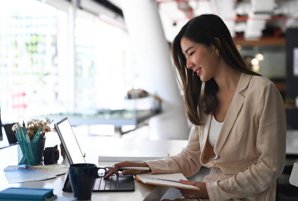 Gülümseyen iş kadınının modern ofiste oturup tablet bilgisayarla çalışmasının yan görünüşü. - Fotoğraf, Görsel