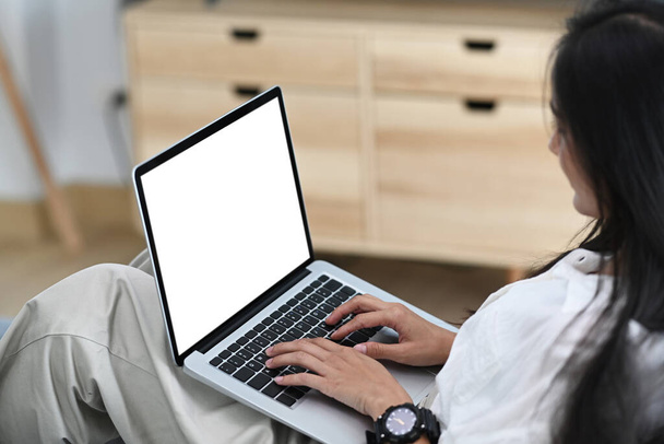 Side view of casual asian woman using laptop while sitting on sofa at home. - Photo, Image