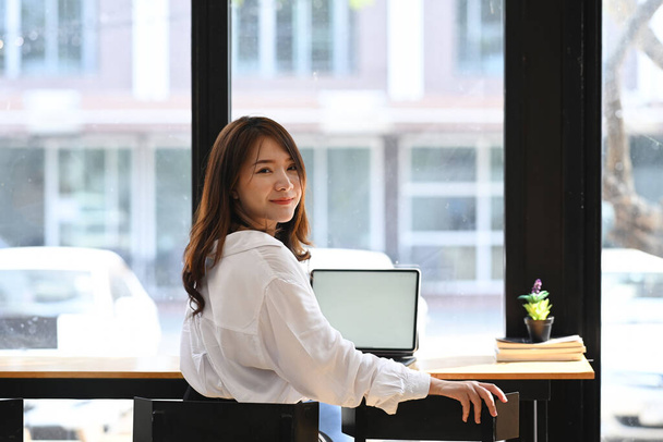 Confident businesswoman sitting near window and looking at camera. - Foto, imagen