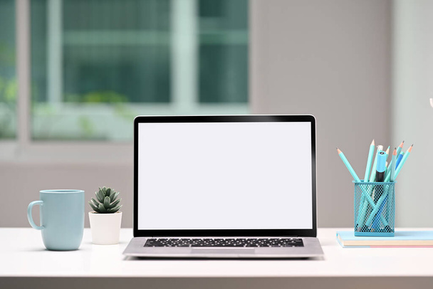 Laptop számítógép, írószer, kávéscsésze és házi növény fehér asztalon, stílusos munkaállomáson. - Fotó, kép