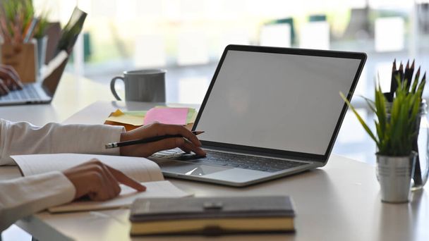 Close-up obraz businesswoman wpisując na białym pustym ekranie laptopa i kopiowanie informacji z dokumentu do laptopa przy nowoczesnym stole roboczym. - Zdjęcie, obraz