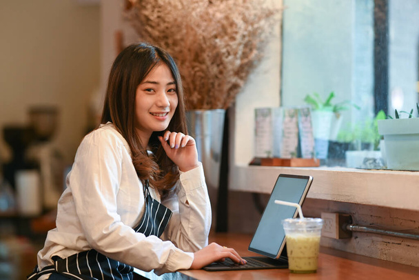 コーヒーショップの中に座ってデジタルタブレットを使用している女性の小さなビジネスオーナーの肖像画. - 写真・画像