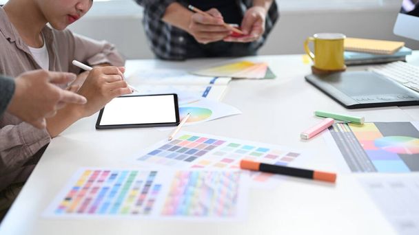 Grupa kreatywnych grafików wybierających kolor z paletą kolorystyczną dla projektu klienta i pracujących z tabletem cyfrowym w sali konferencyjnej.  - Zdjęcie, obraz