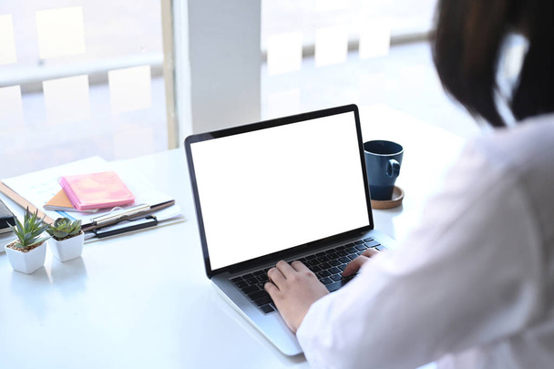 Rückansicht einer Geschäftsfrau oder Büroangestellten, die Daten in ihren Computer-Laptop tippt, um ihren Bericht vorzubereiten . - Foto, Bild