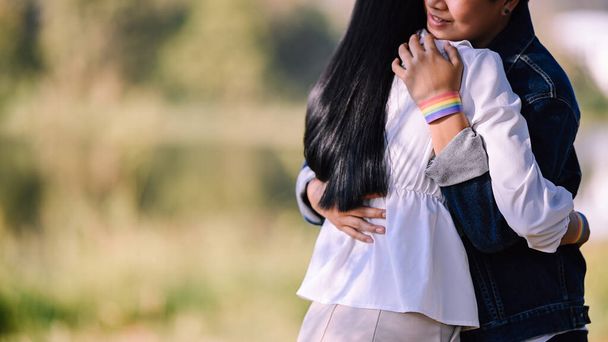 Cropped shot of young LGBT couples while hugging in the park. Behind view of showing LGBT bracelet. LGBT happiness concept. - Photo, Image