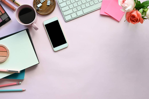 Top view image of woman accessories putting on the pink working desk, including keyboard, coffee cup, bouquet, notebook, pen, mobile, cosmetics and paper clip. Feminine working desk concept. - Photo, Image