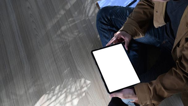 Cropped shot of young man freelance sitting on wooden floor and using digital tablet. - Φωτογραφία, εικόνα