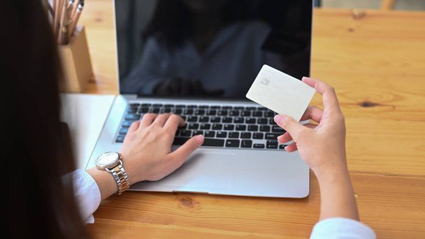 Vista trasera de la joven hembra usando el ordenador portátil y la celebración de pago con tarjeta de crédito en línea o compras en línea. - Foto, imagen