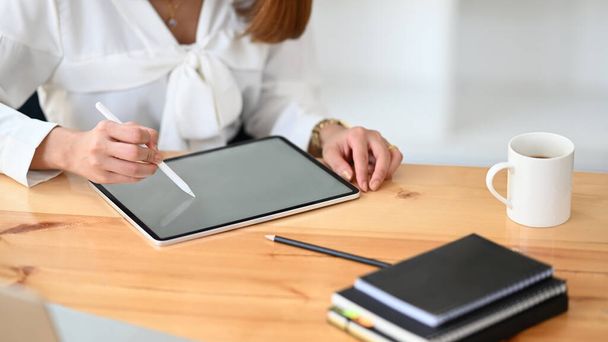 Przycięty wizerunek bizneswoman trzymającej i rysującej na tablecie komputerowym w swoich rękach w nowoczesnym biurze. - Zdjęcie, obraz