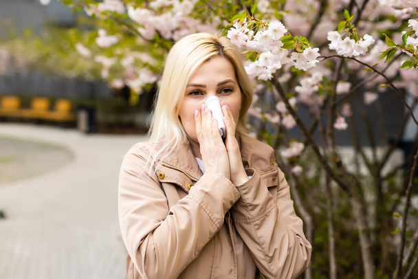 若いきれいな女性が花の木の前でくしゃみをする。春のアレルギーコンセプト - 写真・画像