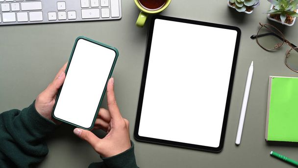 Top view of female hands holding mobile phone and mock up digital tablet on green table. Blank screen for text message or information content. - Photo, Image