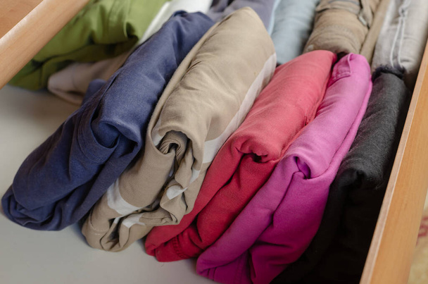 Концепция вертикальной японской системы хранения одежды. Разноцветные рубашки, сложенные в полку комода с помощью метода Konmari уборки. - Фото, изображение