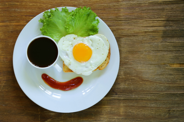grappig gezicht serveert ontbijt, gebakken ei, toast en groene salade - Foto, afbeelding