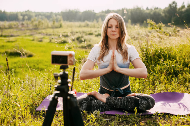 La chica practica yoga en la naturaleza y graba una videolección sobre yoga. Yoga en línea, formación en línea - Foto, imagen