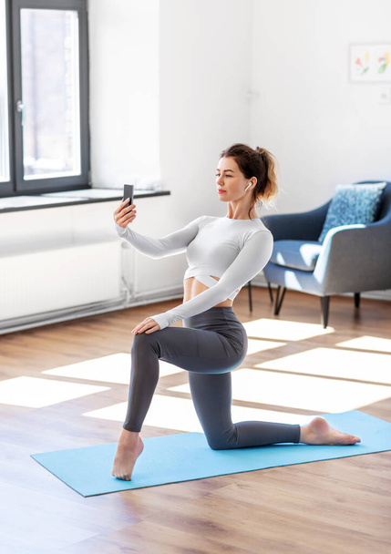 young woman with smartphone doing yoga at home - Foto, imagen