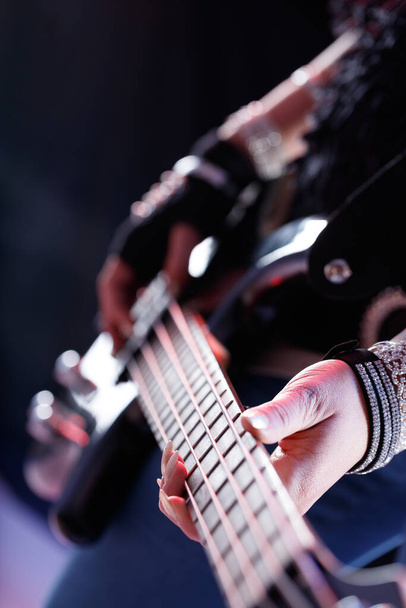 Kobieta muzyk gra na gitarze elektrycznej podczas występu w zbliżeniu na ręce i szyi instrumentu w niskim kluczowym portrecie - Zdjęcie, obraz