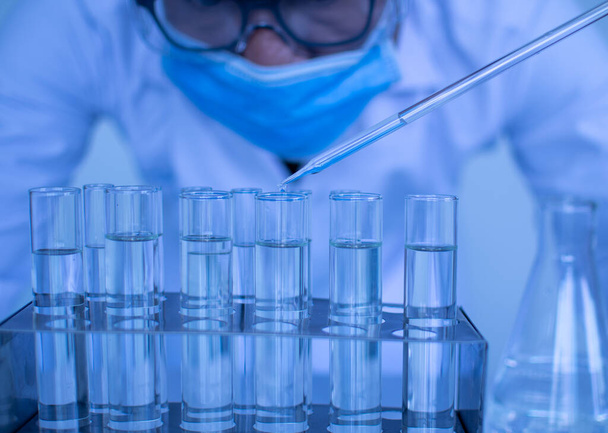 Ein Wissenschaftler mit Schutzbrille und Handschuhen tropft Chemikalien aus, um einen Impfstoff zu testen. Biochemiker führen Experimente durch, um neue Medikamente zu entdecken. Forscher arbeiten in wissenschaftlichen Laboren. - Foto, Bild
